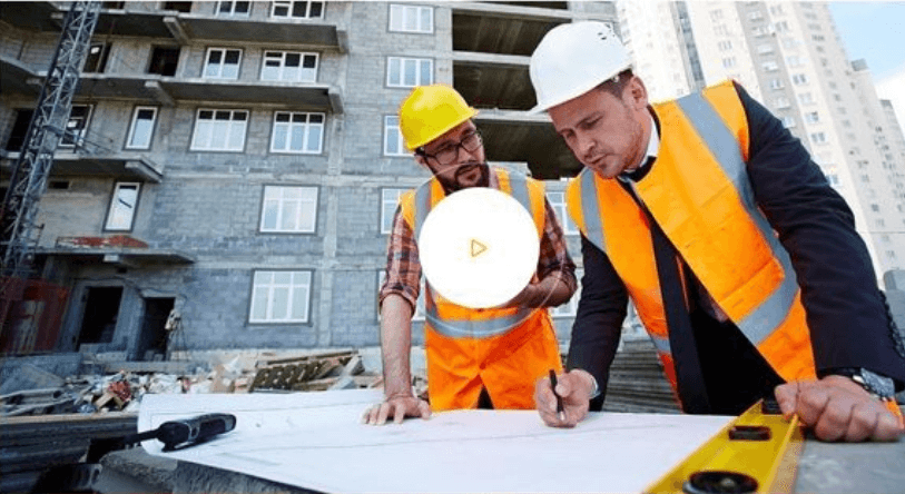 Two engineers marking up a blueprint in front of a building under construction